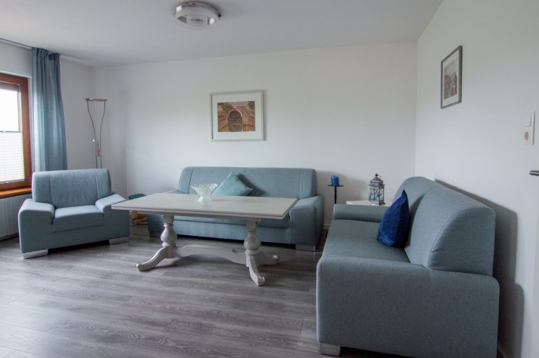 Wohnzimmer mit drei Sofas in hellem blau und einem Couchtisch.